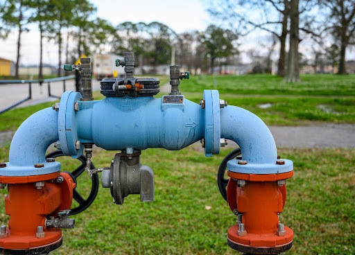 Blue and orange backflow preventer valve assembly installed outdoors on a grassy lawn.