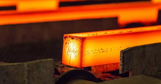 Glowing red-hot square steel billet being processed on a rolling mill line.