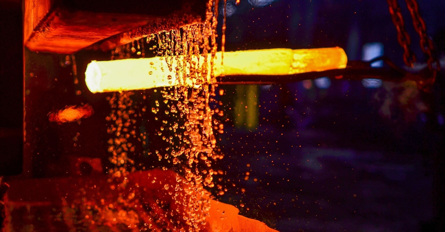 Red-hot metal rod being cooled with water spray during the quenching process in a steel mill.