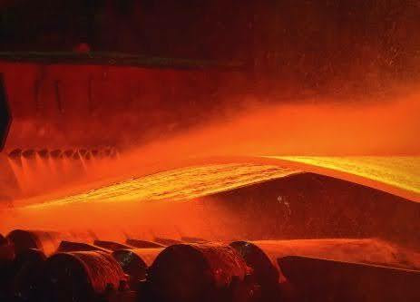 Glowing red-hot steel being processed through industrial heat treating equipment.